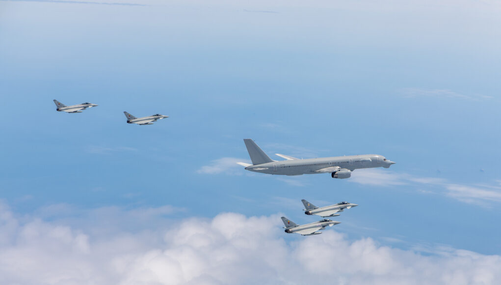RS296216_013A1177_lpr Six gray military fighter jets flying in formation over a blue sky with white clouds.