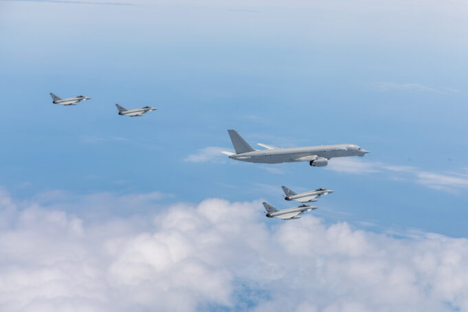 Six gray military fighter jets flying in formation over a blue sky with white clouds.