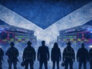 Silhouetted firefighters stand in front of two ladder fire engines with blue emergency lights, against a large Scottish flag backdrop.