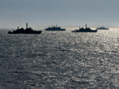 Silhouetted naval ships on a glittering ocean at sunset