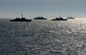 Silhouetted naval ships on a glittering ocean at sunset