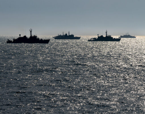 Silhouetted naval ships on a glittering ocean at sunset