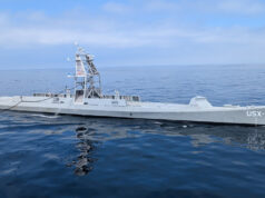 Maritime autonomy: the race is on for the Navy of the future Large gray naval vessel with a tall lattice-like superstructure sailing on calm blue ocean.”