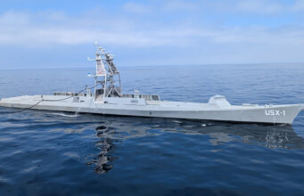 Maritime autonomy: the race is on for the Navy of the future Large gray naval vessel with a tall lattice-like superstructure sailing on calm blue ocean.”