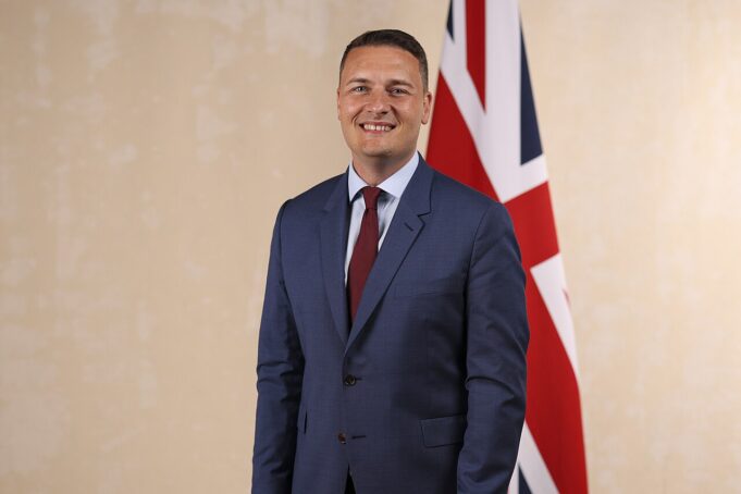 Wes Streeting appointed Defence Secretary Smiling man in a blue suit and red tie standing in front of a British flag.