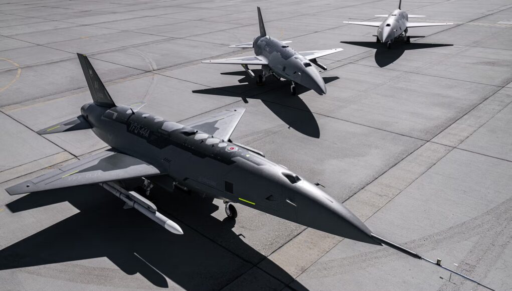 anduril Three military fighter jets parked on a concrete airstrip with their shadows visible on the tarmac, seen from above.