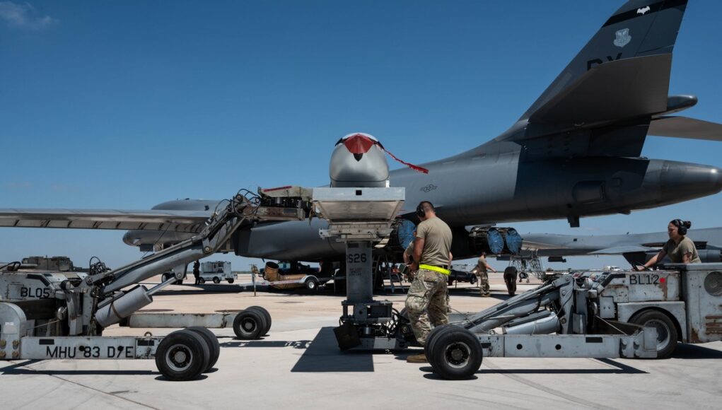 b1 Ground crew service a large military aircraft on a tarmac with loading equipment and vehicles nearby under a clear blue sky.