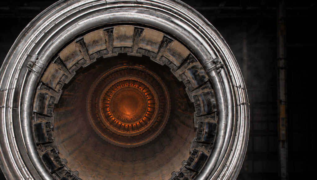 Close-up of a metallic turbine engine, concentric rings framing an orange-hot center, viewed head-on for an industrial feel