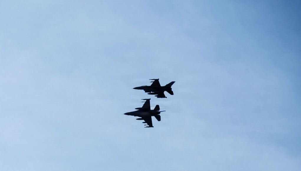 510th & 555th FGS exercise ACE capabilities with Romanian Allies Three silhouetted fighter jets fly in formation across a clear blue sky, with faint reflections below on the water surface.