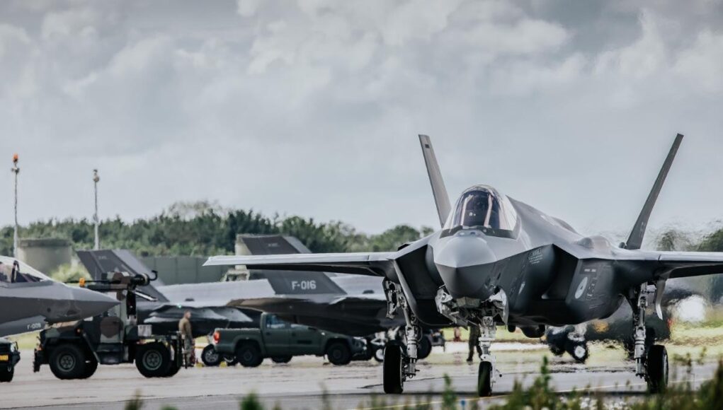 f35 Front view of a stealth fighter on a runway at a military airbase, with ground crew and support vehicles in the background.