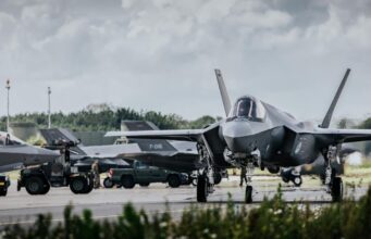 Allied air forces train elite instructors in Netherlands Front view of a stealth fighter on a runway at a military airbase, with ground crew and support vehicles in the background.