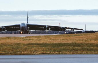 B-52 bomber taxiing on a runway at an airfield, engines visible under its long wings.