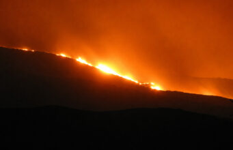 Military aid requested for raging Scottish wildfire Fire rips along a hillside at night, bright orange flames lighting the sky and smoke.