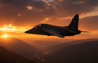 Two-seat military trainer jet silhouetted against a glowing orange sunset over a winding river and mountainous valleys.