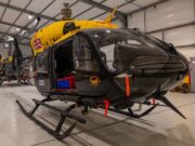 Jupiter helicopters arrive in Cyprus for 84 Squadron Military helicopters in a spacious hangar; a black helicopter in the foreground with a bright yellow top and a Union Jack emblem on its side