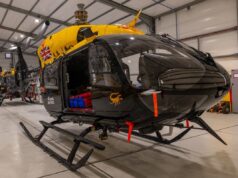 Military helicopters in a spacious hangar; a black helicopter in the foreground with a bright yellow top and a Union Jack emblem on its side