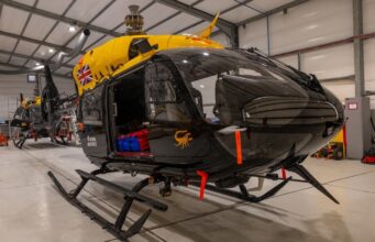 Jupiter helicopters arrive in Cyprus for 84 Squadron Military helicopters in a spacious hangar; a black helicopter in the foreground with a bright yellow top and a Union Jack emblem on its side