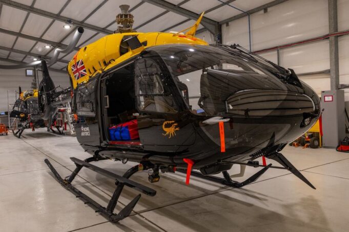 Jupiter helicopters arrive in Cyprus for 84 Squadron Military helicopters in a spacious hangar; a black helicopter in the foreground with a bright yellow top and a Union Jack emblem on its side