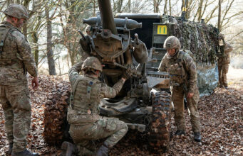 BAE inks deal for Light Gun production inside Ukraine Soldiers in camouflage work on a large artillery piece in a leaf-covered forest.