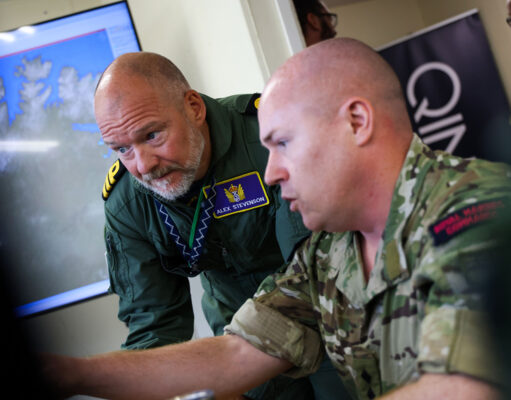 Inside Virtual Warrior – the Royal Navy’s secret war game Two soldiers lean over a desk, examining a large monitor showing a world map in a briefing room.