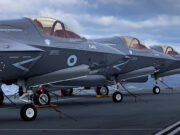 Why the Royal Navy keeps going back to the High North Several gray military fighter jets parked in a row on a ship's flight deck, secured with chains with the ocean in the background.