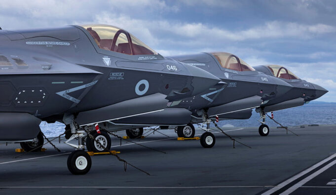Why the Royal Navy keeps going back to the High North Several gray military fighter jets parked in a row on a ship's flight deck, secured with chains with the ocean in the background.