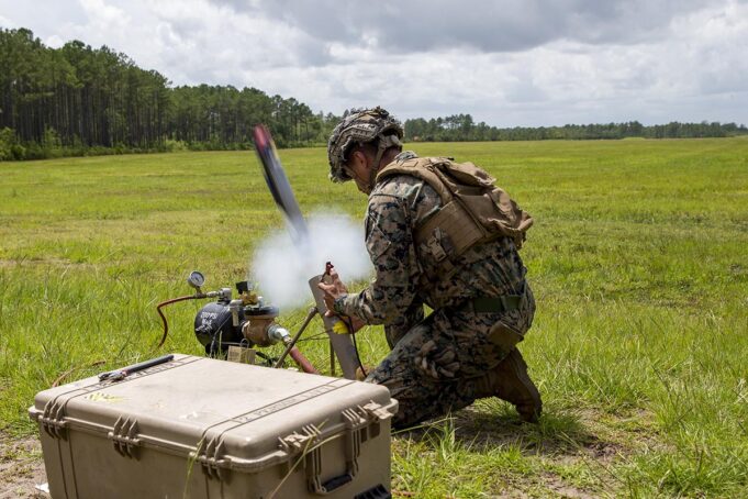 US approves Switchblade drone sale to Greece Soldier in camouflage kneels in a grassy field, handling a portable rocket launcher with a large rugged equipment case nearby.