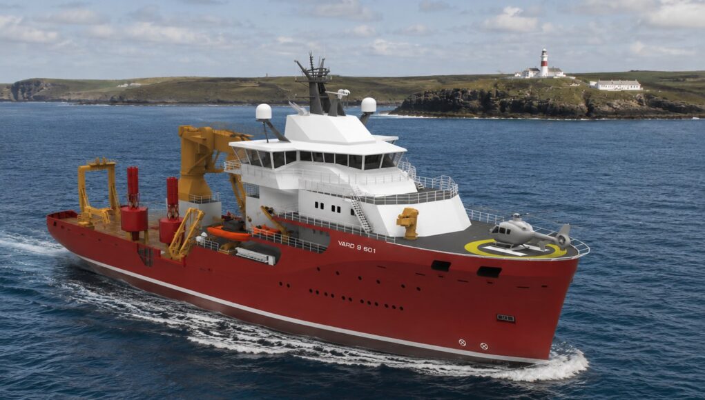 vard3234 Red offshore support vessel with white superstructure and a yellow crane array, moving through open water; helicopter on the forward helipad and a lighthouse visible on a rocky coastline in the background, vessel marked VARD 9 601.