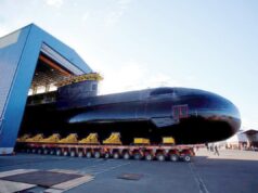 Babcock wins six-year extension for Canada sub support Large black submarine on a long, multi-wheeled transport trailer outside a blue hangar, with workers nearby.