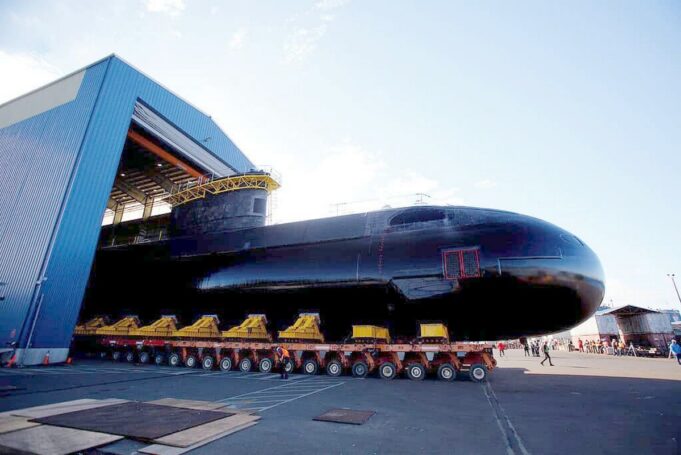 Babcock wins six-year extension for Canada sub support Large black submarine on a long, multi-wheeled transport trailer outside a blue hangar, with workers nearby.