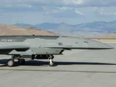 New American combat drones armed and flown in desert Close-up side view of a gray military jet on a taxiway, with arid mountains in the distance under a blue sky with clouds.