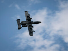British controllers direct A-10 strikes Underside view of a gray four-engine propeller aircraft (C-130) flying overhead against a blue sky.