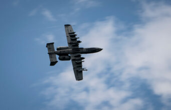 British controllers direct A-10 strikes Underside view of a gray four-engine propeller aircraft (C-130) flying overhead against a blue sky.