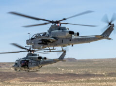 US Marine Corps gunships to get Link 16 upgrade Two US Marine Corps helicopters hovering low over a desert landscape with blurred rotor blades and a visible American flag decal on one side.