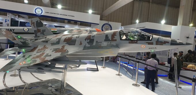 Rolls-Royce and Reliance plan Indian fighter engine Side view of a camouflaged fighter jet on display at an air show exhibit, with cockpit visible and visitors nearby.