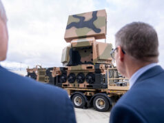 Britain moves closer to buying Australian radar Two men in suits watch a camouflaged mobile artillery/launcher mounted on a large wheeled transport truck outdoors