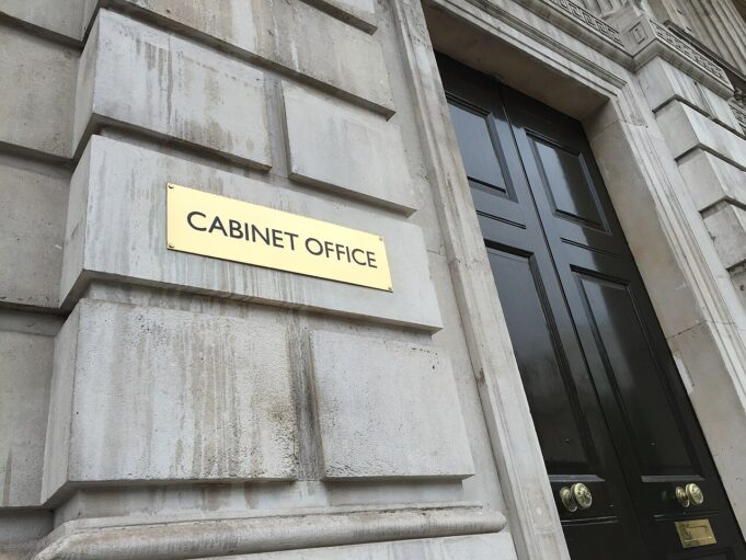 Gold plaque reading 'CABINET OFFICE' mounted on a weathered stone wall beside a tall black door with brass handles.