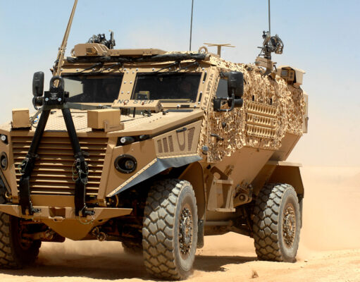 Hybrid Foxhound and Boxer could carry lasers, paper says Desert armored military vehicle in tan camouflage on sandy terrain under a clear blue sky, front view showing heavy tires and equipment on the hood and sides.