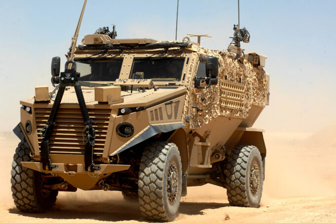 Hybrid Foxhound and Boxer could carry lasers, paper says Desert armored military vehicle in tan camouflage on sandy terrain under a clear blue sky, front view showing heavy tires and equipment on the hood and sides.