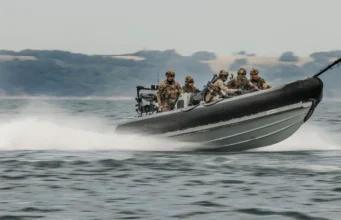 Korean special forces train with Royal Marines in UK first Six soldiers in camouflage gear on a high-speed inflatable military boat skimming over the water with a misty shoreline in the background.