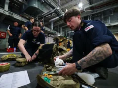 First combat medic course run aboard a Royal Navy ship British Royal Navy personnel kneel on a hangar deck, organizing and packing medical supplies from tactical bags for a field drill or mission.