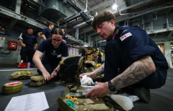 British Royal Navy personnel kneel on a hangar deck, organizing and packing medical supplies from tactical bags for a field drill or mission.