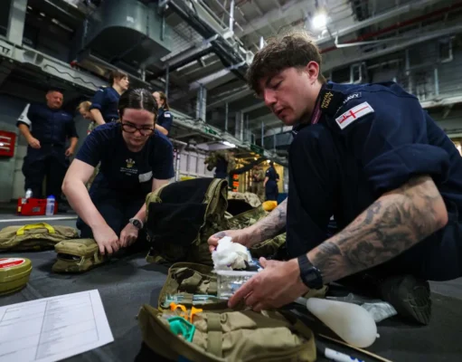 British Royal Navy personnel kneel on a hangar deck, organizing and packing medical supplies from tactical bags for a field drill or mission.