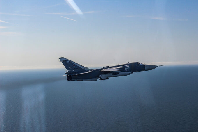 NATO jets scrable to intercept Russian bombers over Baltic Blue military fighter jet with the number 02 flying over the calm ocean against a clear blue sky, navy-gray livery visible on the fuselage and tail insignia clearly shown.