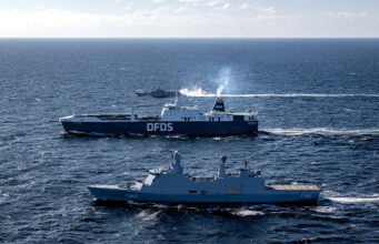 Two large ships sail on open sea, a blue DFDS ferry behind a gray military vessel labeled F342.