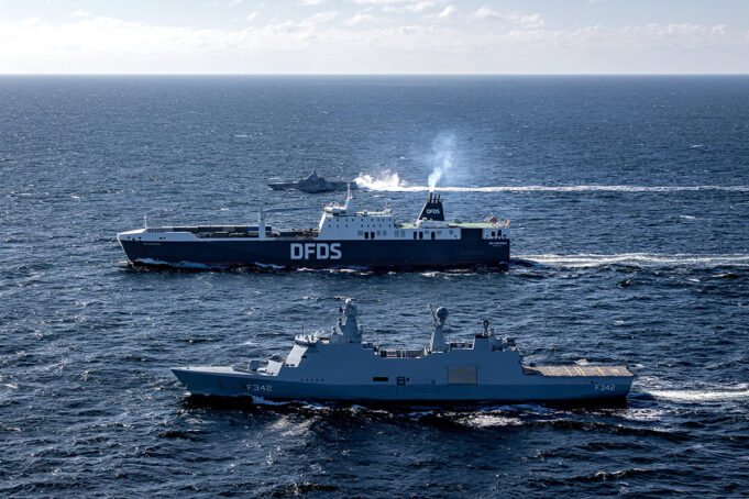 Two large ships sail on open sea, a blue DFDS ferry behind a gray military vessel labeled F342.