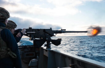 British warship opens fire near Falklands to deter Argentina Sailors on a naval deck firing a large mounted gun, muzzle flash over the ocean with a cloudy sky behind.