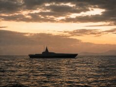 Britain to buy new drone warfare testbed vessel Silhouette of a modern motor yacht on the sea at sunset with an orange sky and distant horizon.