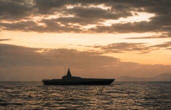 Britain to buy new drone warfare testbed vessel Silhouette of a modern motor yacht on the sea at sunset with an orange sky and distant horizon.