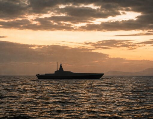 Britain to buy new drone warfare testbed vessel Silhouette of a modern motor yacht on the sea at sunset with an orange sky and distant horizon.